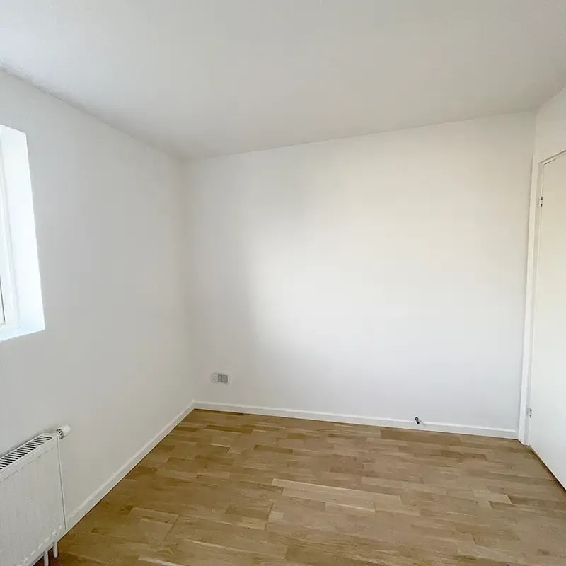 Nymalet hvidt værelse med lyst trægulv, radiator og vindue