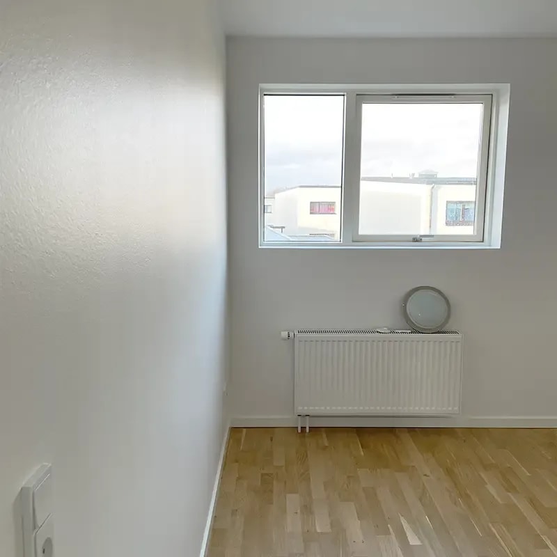 Nymalet værelse med hvidt vindue, radiator og lyst trægulv